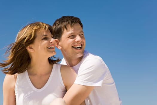 Portrait of cheerful couple looking aside against blue sky