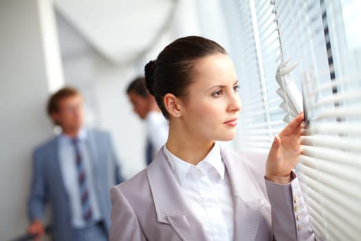 Businesswoman looking through window against her colleagues