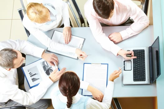 Above view of four businesswomen sitting at table and pointing at the laptop screen