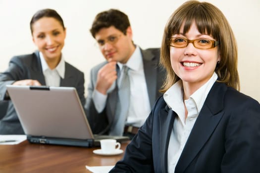 Smart woman in glasses smiles on a background of her the coworkers in the office
