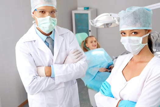 Portrait of pretty assistant and dentist in masks looking at camera in dentistry office