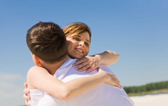 Portrait of amorous couple embracing against blue sky at summer