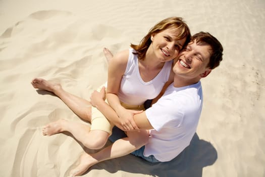 Portrait of amorous couple embracing while sitting on sand