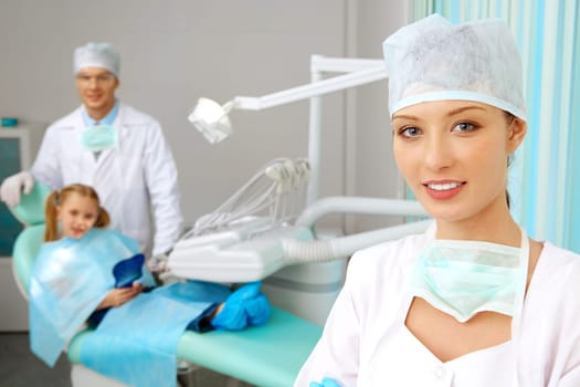 Beautiful woman in uniform looking at camera with smile on background of doctor and patient