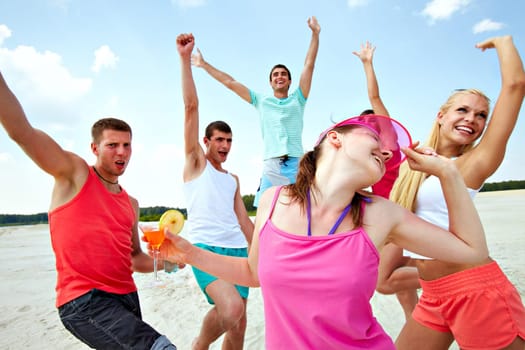 Six joyful friends dancing on beach during vacation