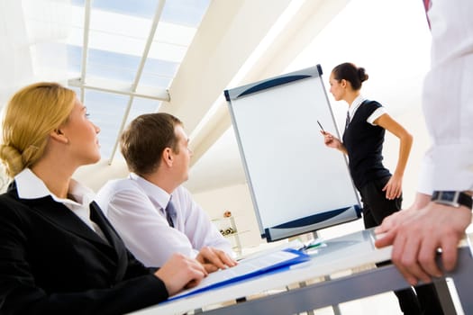 Photo of successful manager standing by whiteboard while the others listening to her