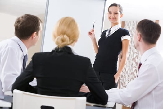 Photo of successful manager standing by whiteboard while the others listening to her