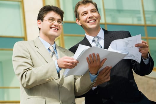 Two businesspeople holding papers looking towards and business center with glassy walls on the background