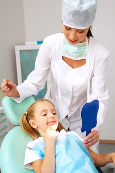 Photo of happy girl looking at her teeth in the mirror with helpful assistant near by