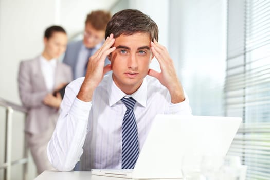 Stressed businessman sitting at table and looking at camera