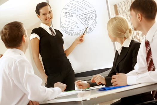 Photo of successful female standing by whiteboard while explaining her idea to colleagues
