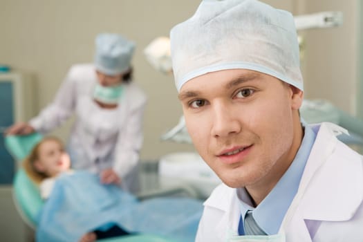 Portrait of confident doctor on background of his assistant with patient