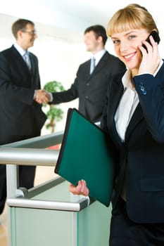 Image of confident woman holding the folder and phone on the background of people shaking hands