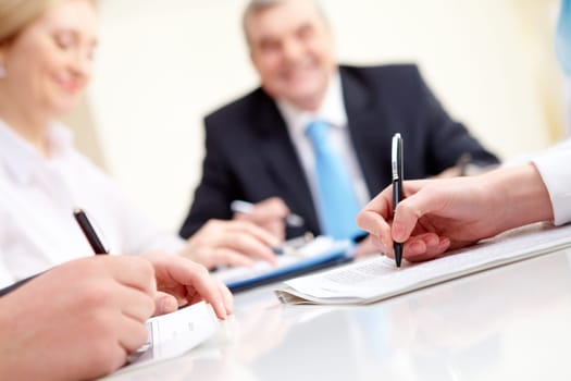 Close-up of business partners hands over document with their boss on background