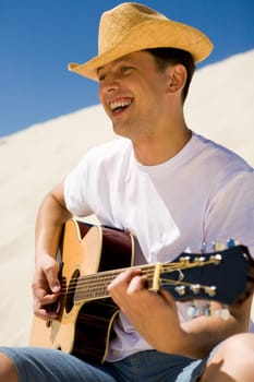 Portrait of handsome man in cowboy hat playing the guitar and singing something on sunny day
