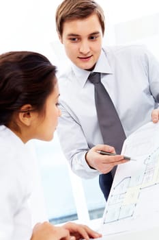 Smart businessman pointing at paper and looking at pretty employee in office