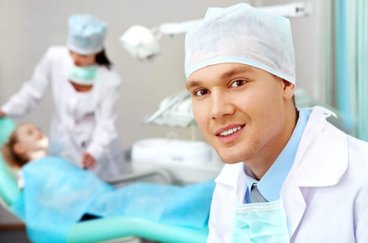 Portrait of confident doctor on background of his assistant with patient