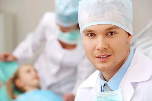 Portrait of young dentist on background of his assistant and patient