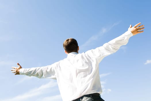 Photo of businessman standing with his arms stretched on the background of blue sky