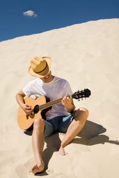 Portrait of happy man in cowboy hat playing the guitar on sandy beach