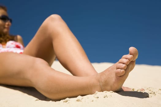 Image of sole of woman lying on sandy beach while sunbathing