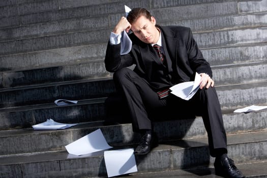 Portrait of sad businessman sitting on stairs with papers in hands and lost expression on his face