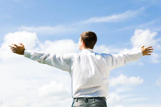 Image of businessman standing aback and looking at blue sky in summer