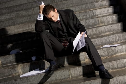 Photo of sad man with papers in hands sitting on stairs with no idea what to do