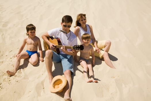 Image of cheerful man playing the guitar with his sons and wife near by