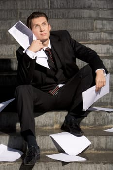 Portrait of depressed manager sitting with papers in hands and around him while looking slightly upwards