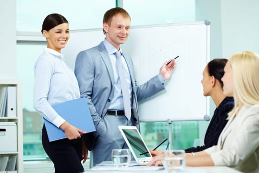 A business man explaining something on a whiteboard with pretty woman near by