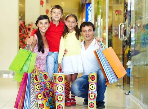 Portrait of a nice family of four with shopping bags looking at camera and smiling