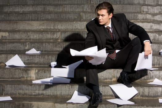 Photo of attractive businessman sitting in frustration with papers in hands