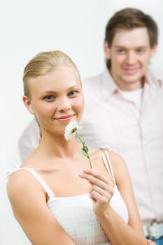 Image of cute girl with white flower looking at camera on background of her boyfriend