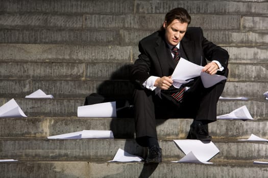 Portrait of depressed employee sitting in frustration on stairs with papers in hands