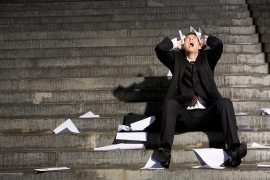 Despaired businessman screaming with papers in hands while sitting on staircase