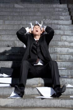 Despaired businessman screaming with papers in hands while sitting on staircase