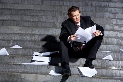 Portrait of depressed employee sitting in frustration on stairs with papers in hands