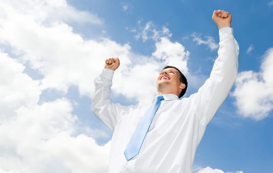 Portrait of happy businessman raising his hands with cloudy sky above him