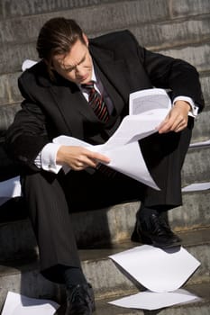 Photo of man reading documents with pensive expression while sitting on staircase