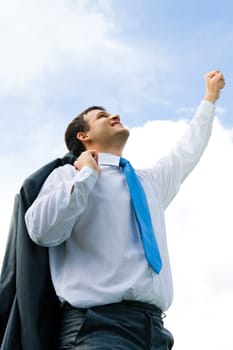 Portrait of young successful businessman raising his fist upwards to the sky and looking at it
