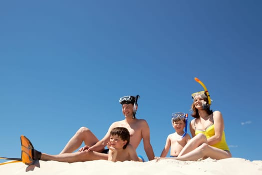Portrait of modern family sitting on sandy beach against blue sky