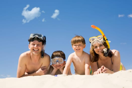 Portrait of diving family lying on sand against blue sky and smiling at camera