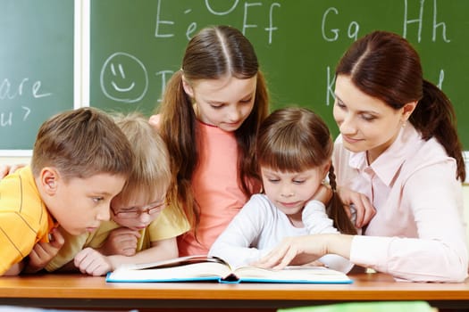 Portrait of smart schoolchildren and their teacher reading book in classroom