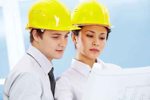 Portrait of two architects in helmets looking document at meeting