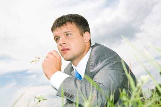 Close-up of pensive businessman with blade in his mouth looking somewhere with sky above him