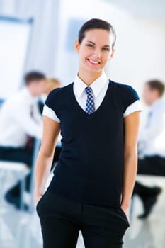 Photo of happy businesswoman in elegant clothing posing before camera with colleagues working behind her