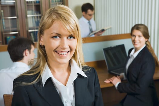 Young beautiful smiling woman in a working environment on a background of her business team
