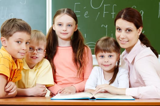Portrait of smart schoolchildren and their teacher looking at camera in classroom