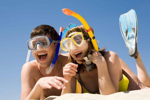 Portrait of cheerful couple in aqualungs lying on sand and laughing